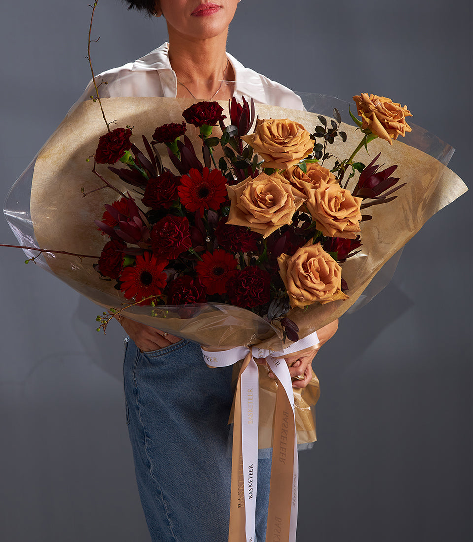 Luxury red gerbera and golden-orange rose bouquet wrapped in kraft paper with gold ribbon