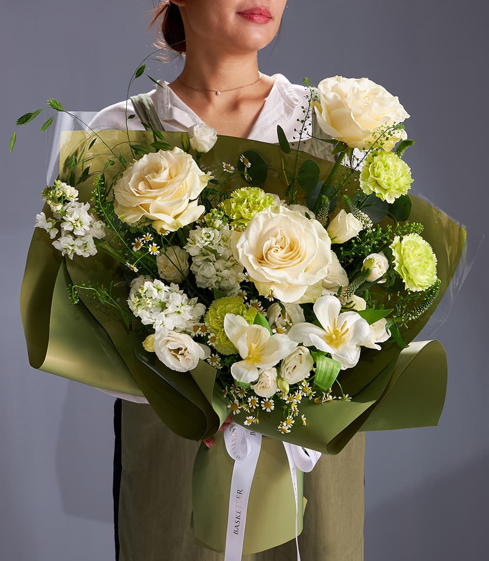 Cream roses and green carnation bouquet with white blooms and fresh greenery, wrapped in green paper