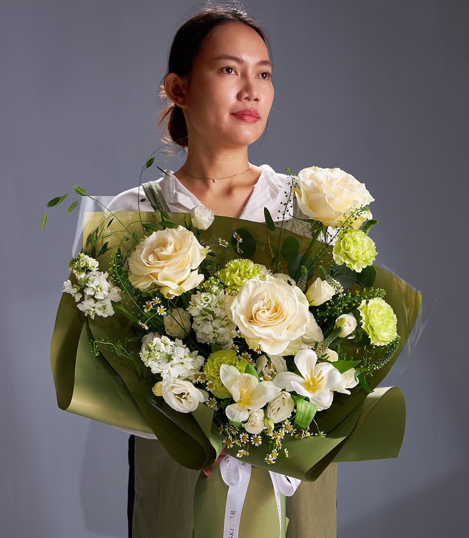 Cream rose and green carnation bouquet with white blossoms and eucalyptus foliage, wrapped in olive kraft paper