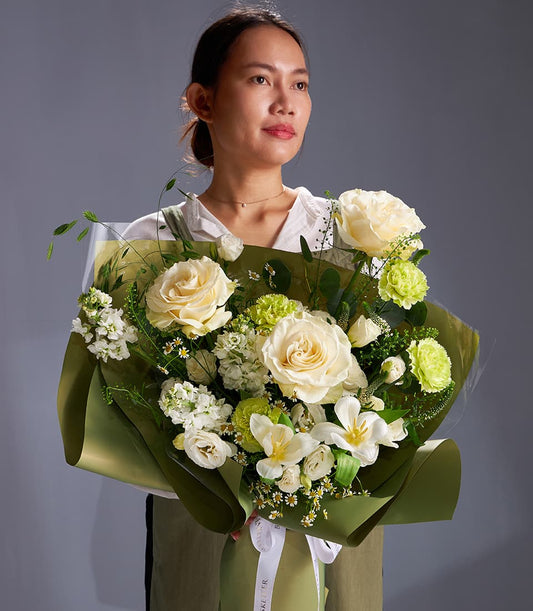 Cream rose and green carnation bouquet with white blossoms and eucalyptus foliage, wrapped in olive kraft paper