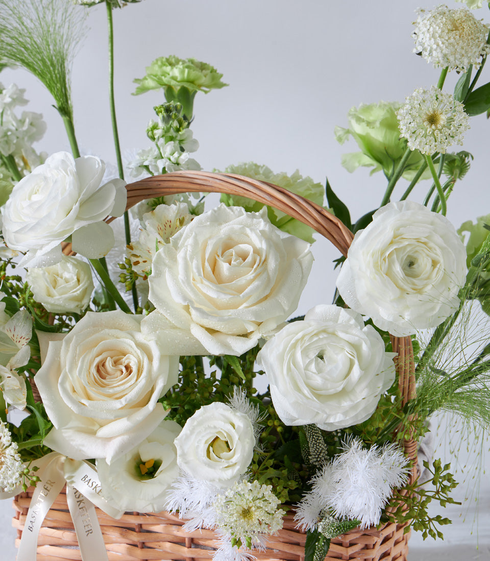 White rose and ranunculus birthday flower basket with woven wicker base and fresh greenery accents