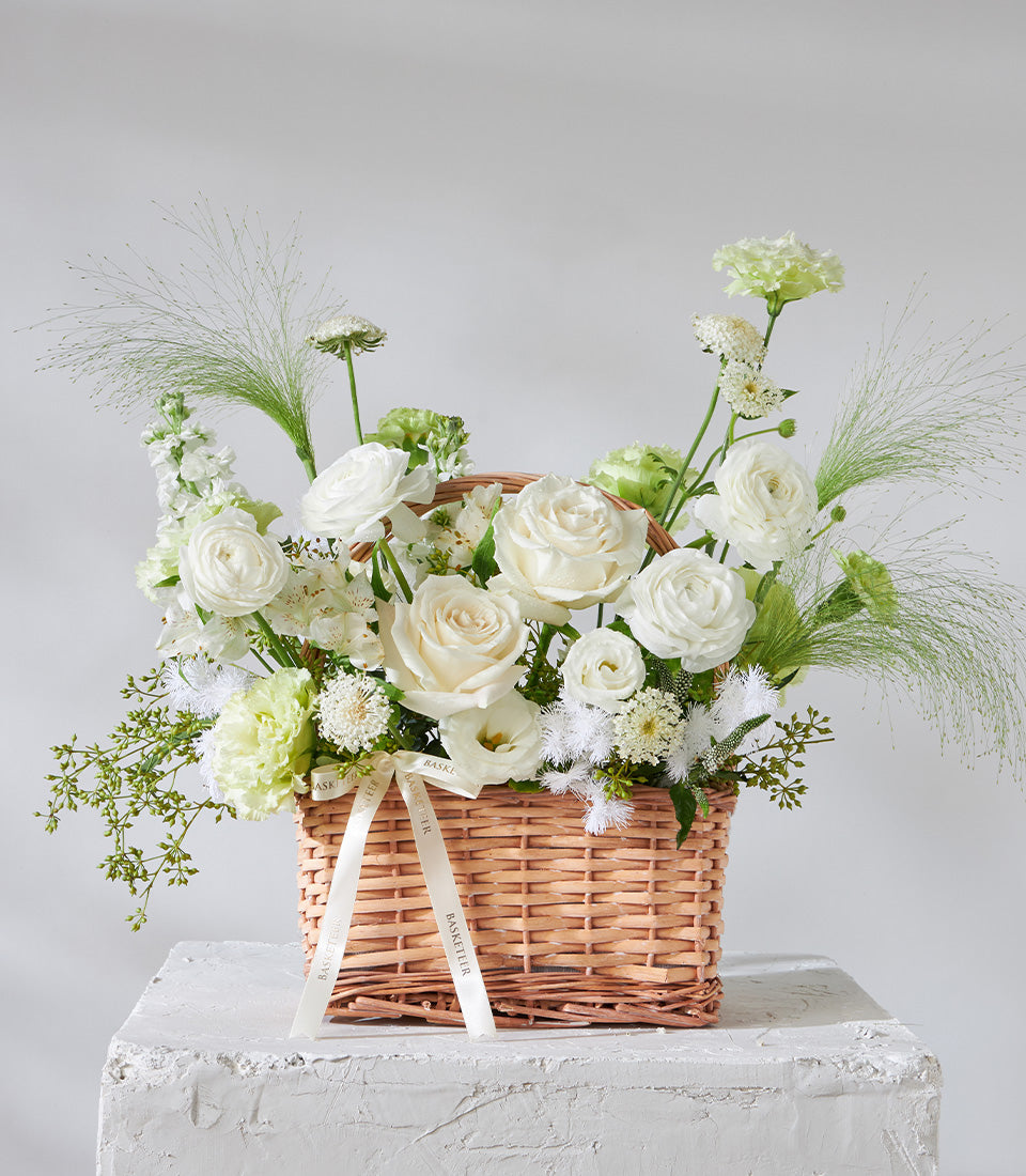White rose and ranunculus birthday flower basket with green foliage in woven wicker