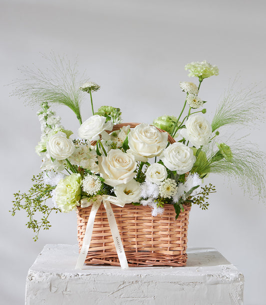White rose and ranunculus birthday flower basket with green foliage in woven wicker