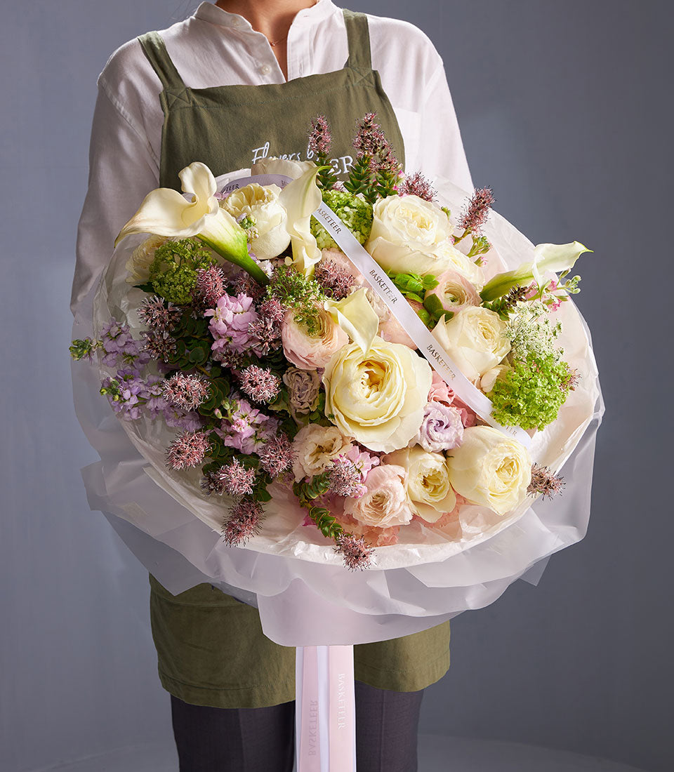 Elegant ivory rose and calla lily bouquet with blush garden roses and purple accent flowers in soft tissue wrapping