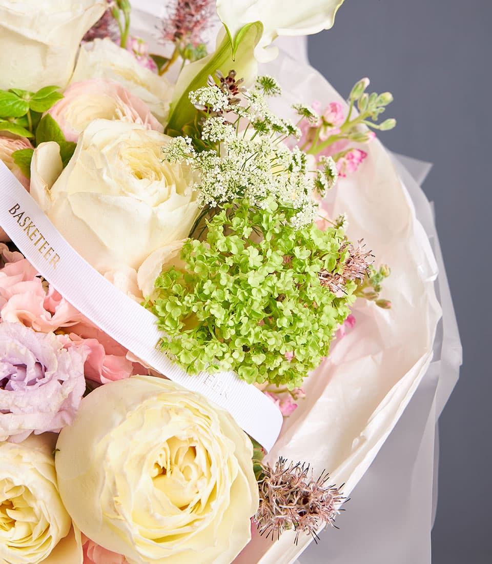 Ivory roses and calla lilies bouquet with pink lisianthus and green foliage, wrapped in white paper