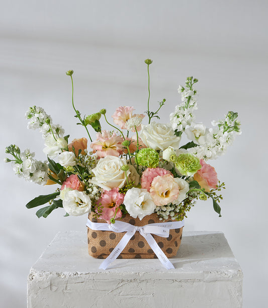 Pastel white roses and peach lisianthus arrangement in polka-dot burlap basket, perfect birthday flower gift