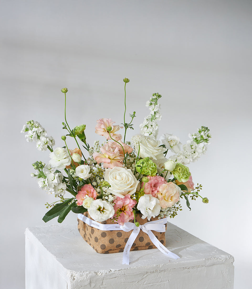 White roses and peach lisianthus flower basket with cream ribbon for birthday gifts