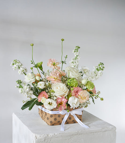 White roses and peach lisianthus flower basket with cream ribbon for birthday gifts