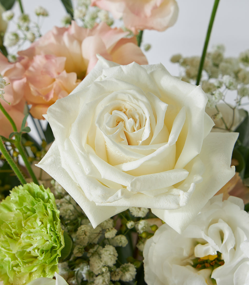 Pastel white roses and peach lisianthus fresh flower arrangement in a wicker basket for birthdays
