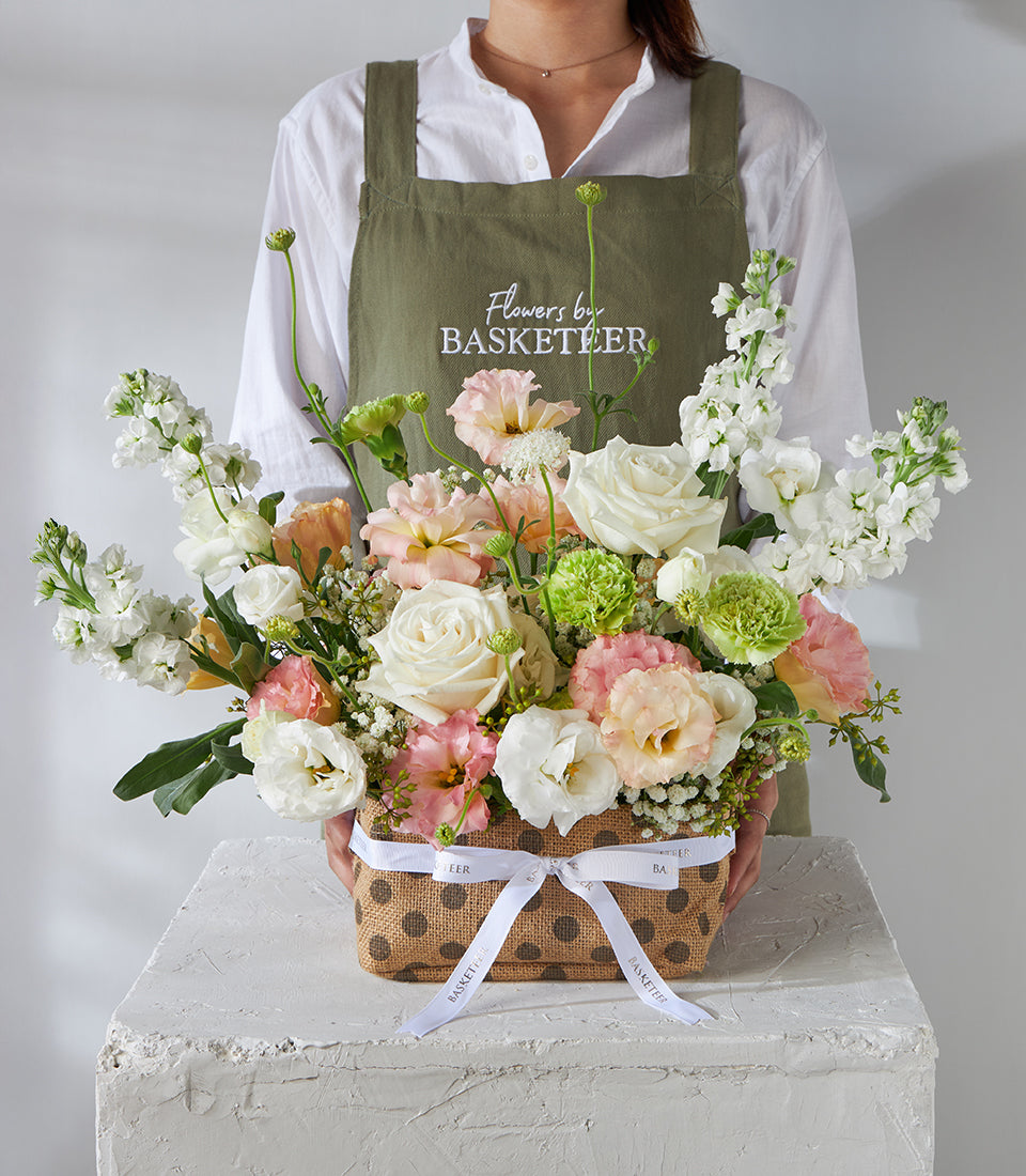 White and peach lisianthus pastel flower basket with roses and greenery, presented in polka dot burlap container with white