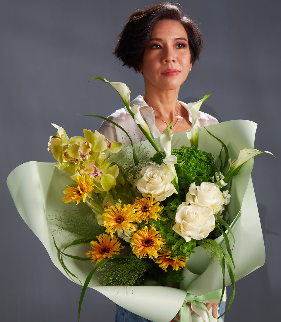 Luxury green and yellow fresh flower bouquet with orchids, roses, and gerbera daisies in mint wrap