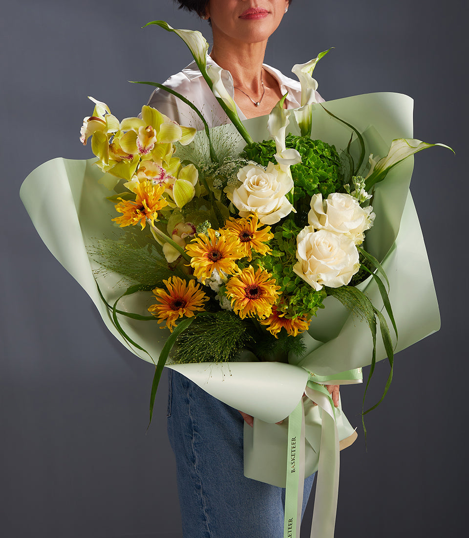 Vibrant yellow and white luxury flower bouquet with orchids, sunflowers, roses and calla lilies in green wrap