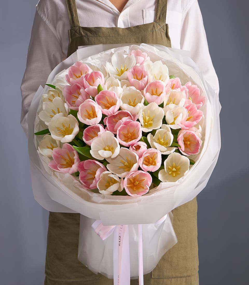 Fresh white and pastel pink tulip bouquet with yellow centers, wrapped in white paper and pink ribbon