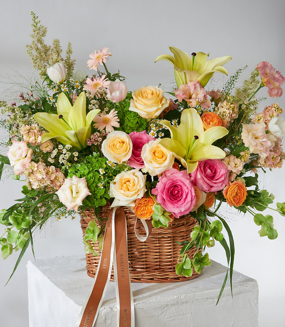 Fresh yellow lilies and pink roses in woven basket with mixed blossoms and greenery