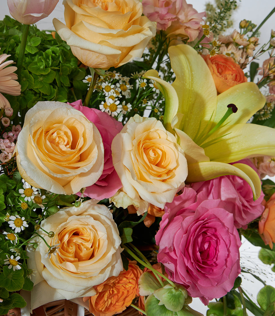 Yellow lilies and pink roses in woven pastel flower basket with cream blooms and foliage