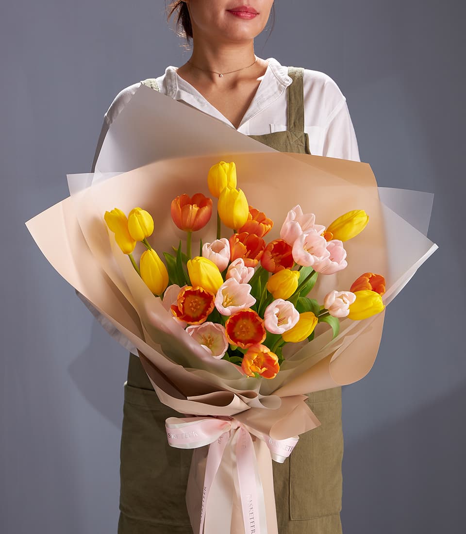 Fresh yellow, orange and blush tulip bouquet with layered paper wrapping and pink ribbon