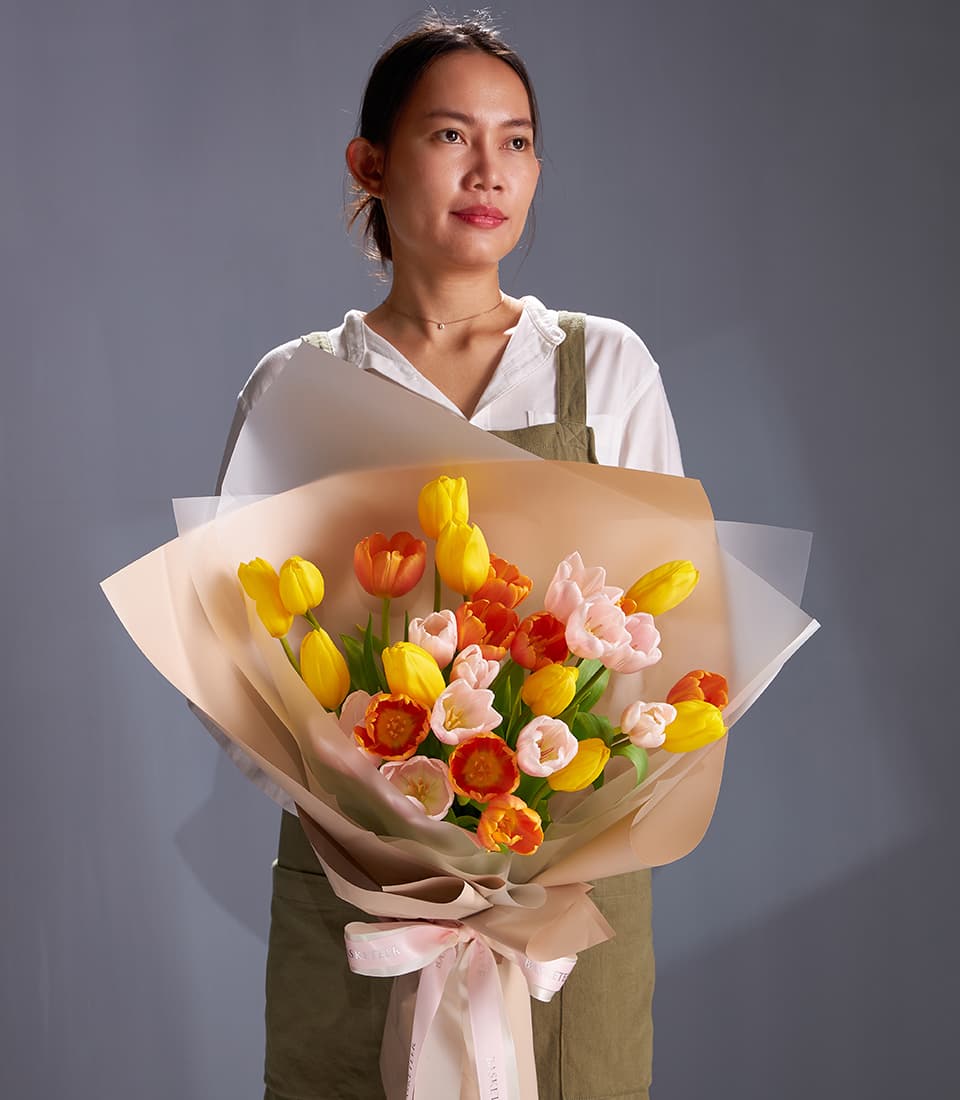 Yellow, orange and blush tulip bouquet in white and peach paper with pink ribbon