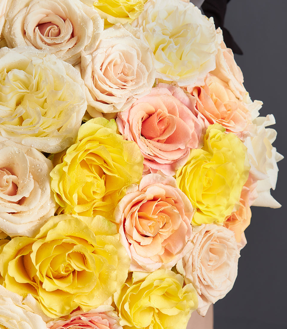 Vibrant yellow, peach, and cream fresh rose bouquet with dark ribbon accent