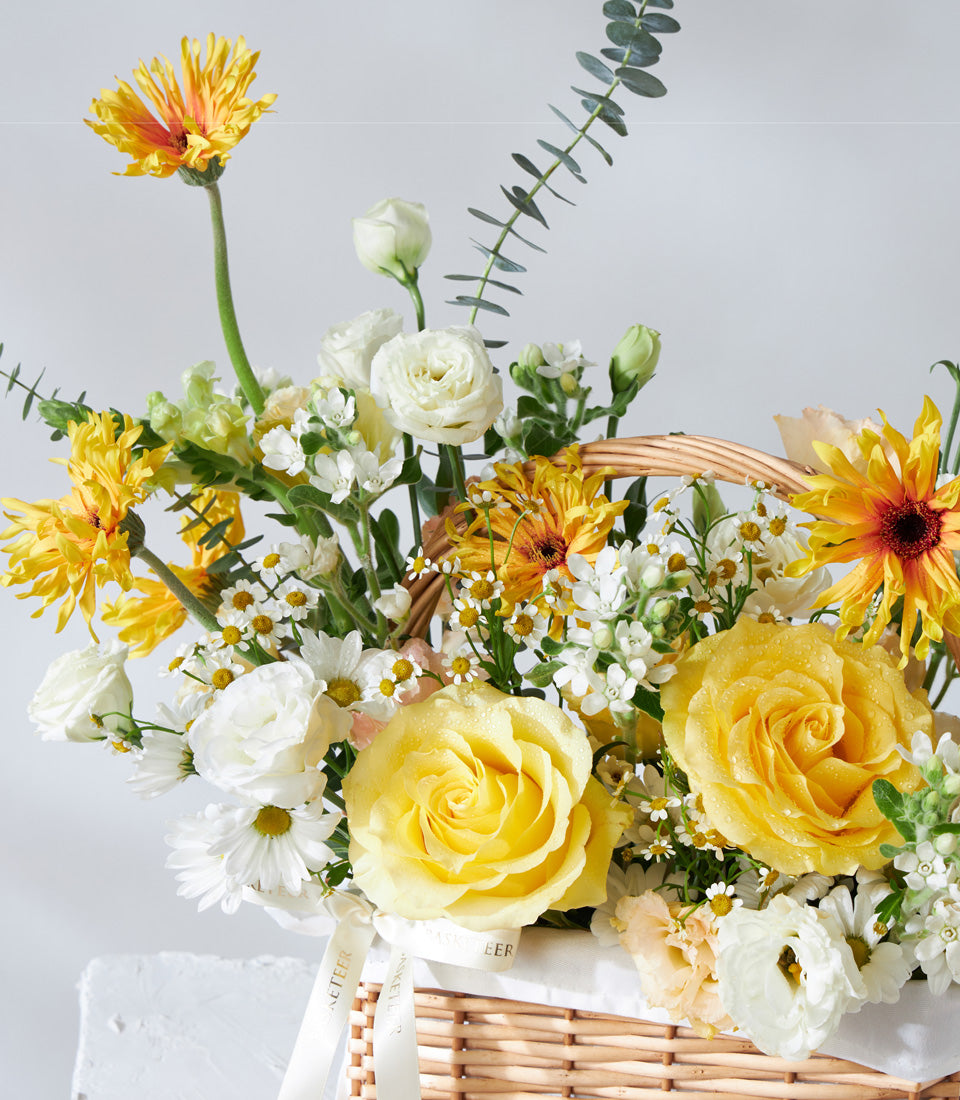 Vibrant yellow and white roses with ranunculus in a woven wicker basket, fresh birthday flowers with eucalyptus greenery