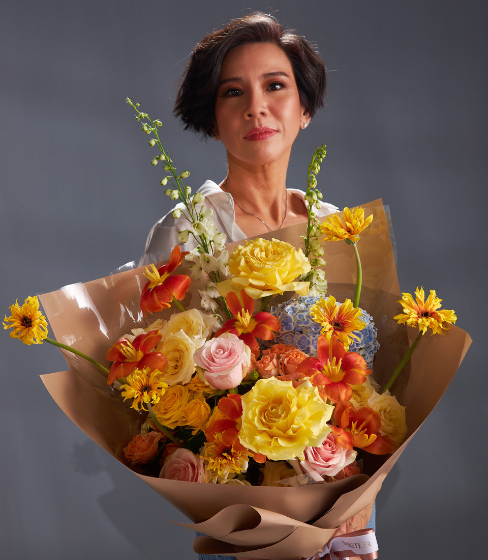 Vibrant mixed rose, lily, and hydrangea bouquet wrapped in brown paper with white ribbon