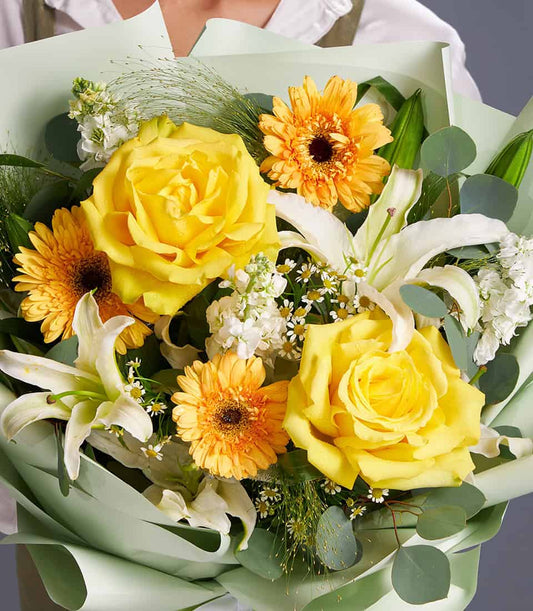 Vibrant yellow roses, white lilies and orange gerberas wrapped in soft mint paper with eucalyptus greenery