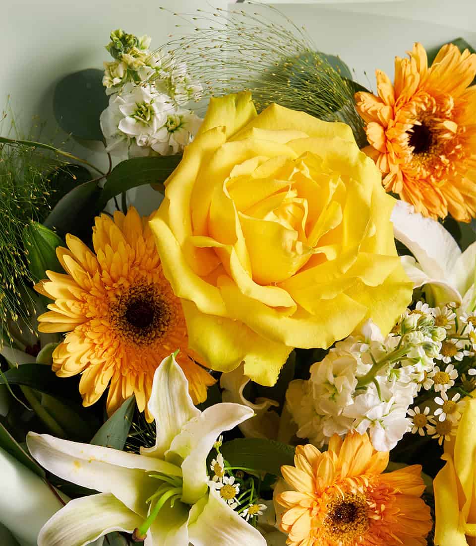 Vibrant yellow roses, white lilies and orange gerberas fresh flower bouquet with greenery