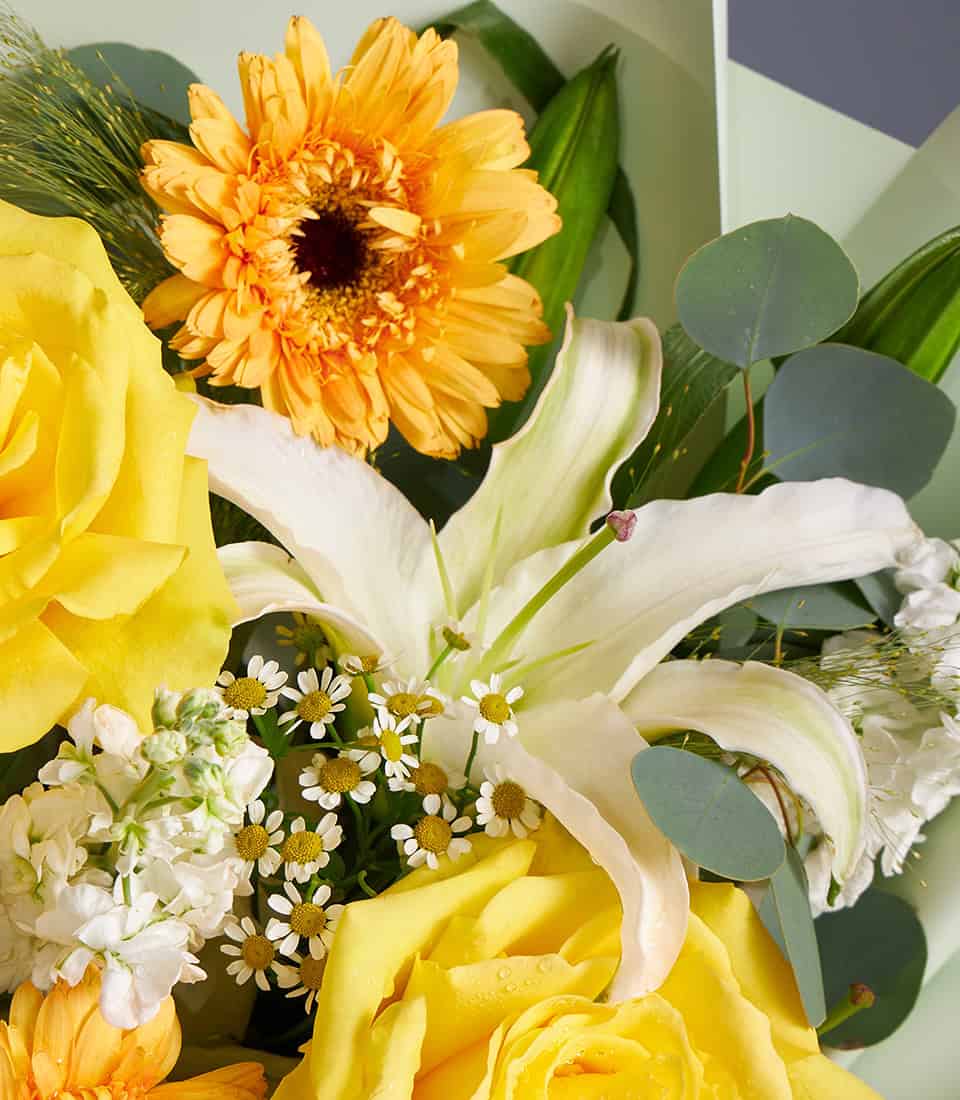Vibrant yellow roses, white lilies, and orange gerbera bouquet with fresh eucalyptus greenery