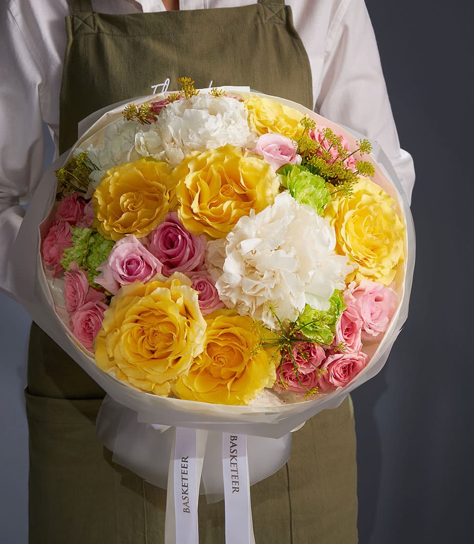Golden mixed bouquet with yellow and pink roses, white carnations, and green filler in white wrapping