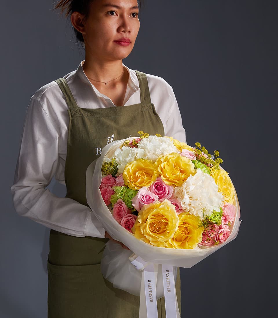 Premium yellow and pink rose bouquet with white carnations and lush green foliage, wrapped in white paper