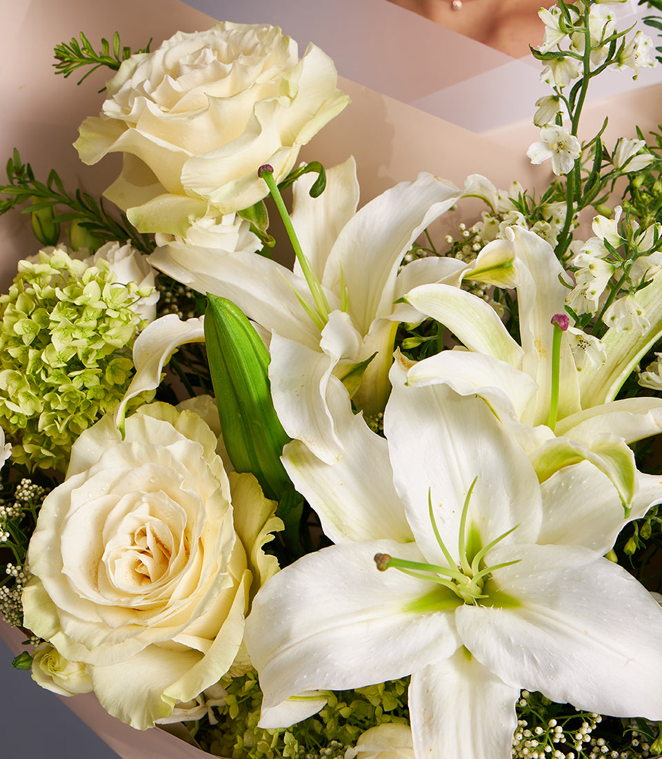 Fresh white lily and cream rose bouquet with green hydrangea, wrapped in soft pink paper