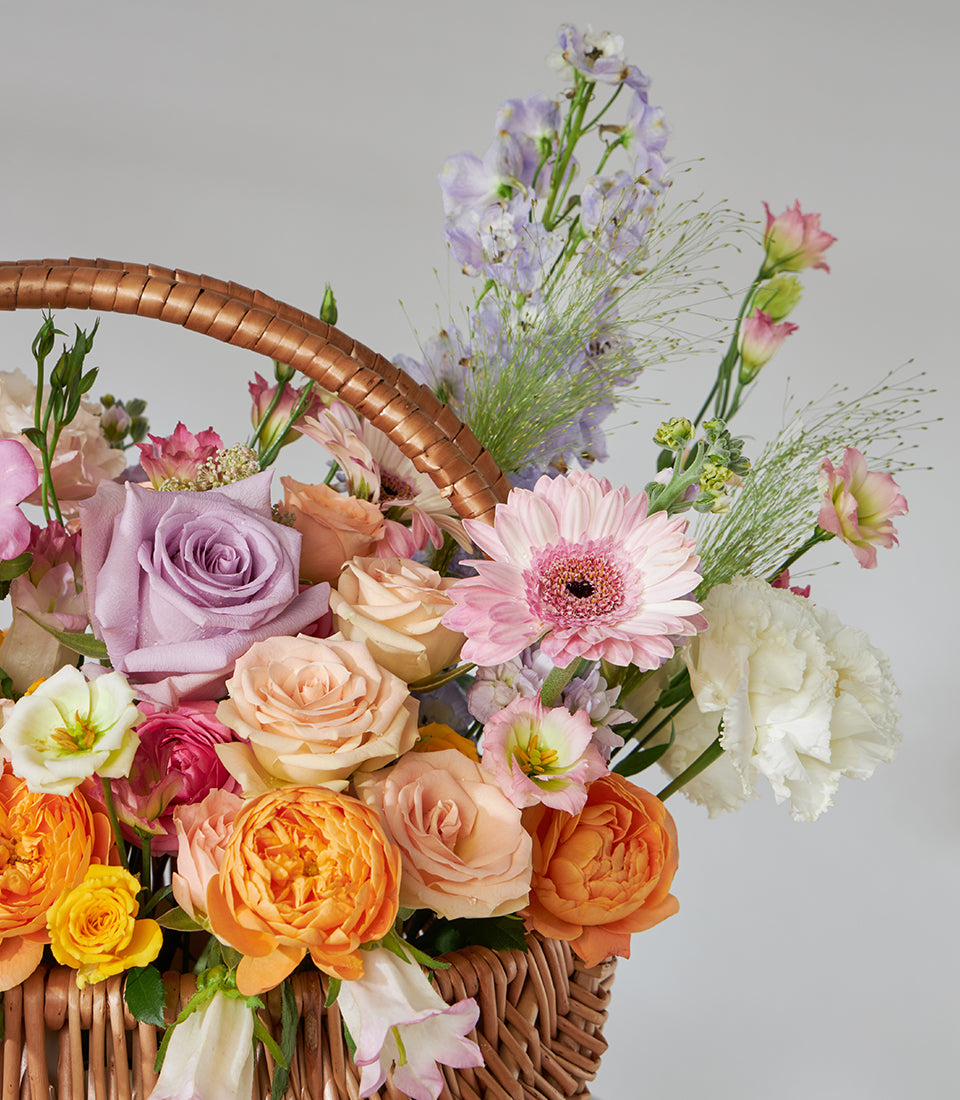 Lavender and peach roses with pink daisies in woven wicker basket arrangement