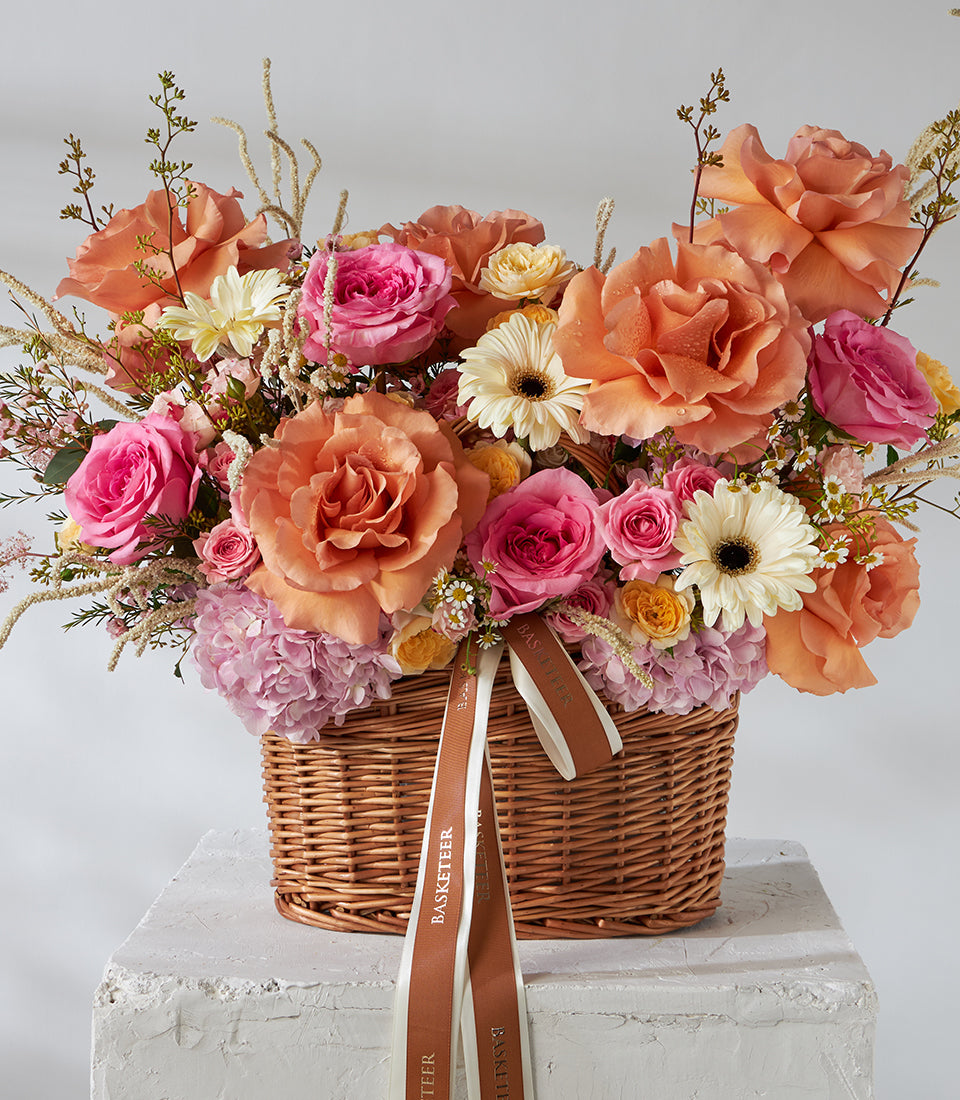 Vibrant orange and pink roses with gerbera daisies in woven wicker basket arrangement