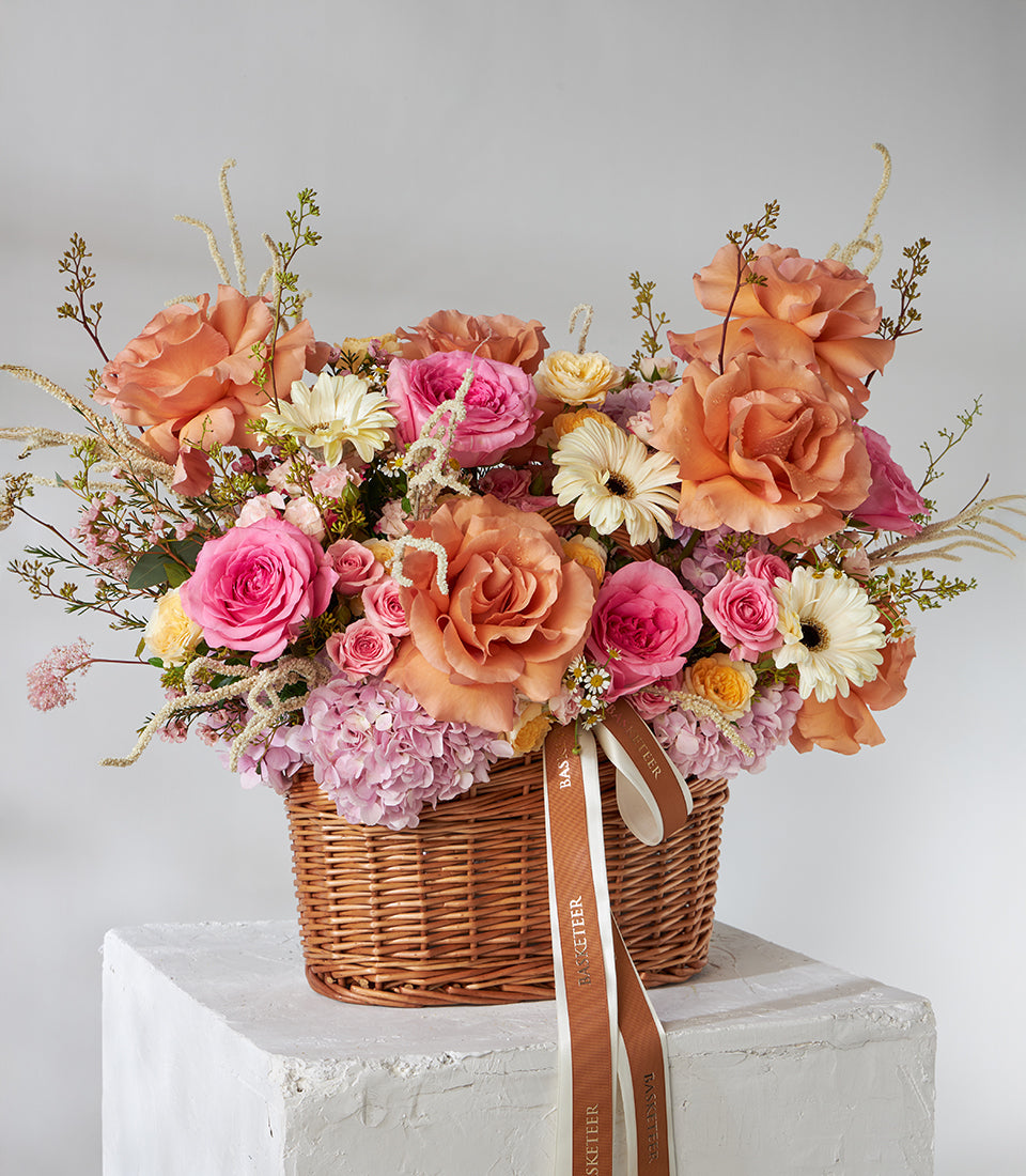 Vibrant orange, pink, and peach rose and gerbera basket bouquet in woven wicker with hydrangeas
