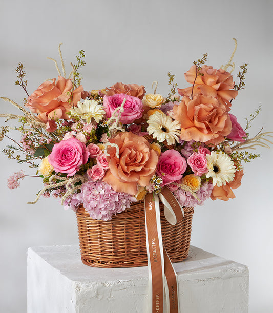 Vibrant orange, pink, and peach rose and gerbera basket bouquet in woven wicker with hydrangeas