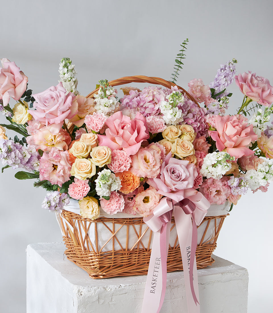 Pastel pink and cream roses with hydrangeas in woven wicker basket, tied with pink ribbon