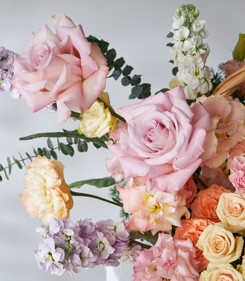 Pastel roses and hydrangeas in soft pink, lavender, and cream arranged in a luxury gift basket with eucalyptus