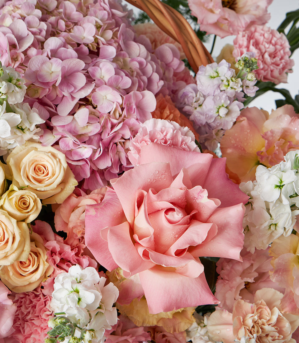 Pastel roses and hydrangeas in a woven basket bouquet with cream and pink blooms