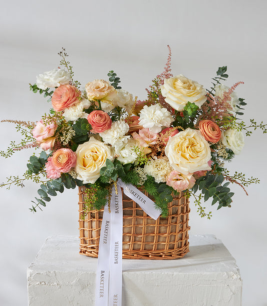 Peach and cream roses with white carnations in woven wicker basket