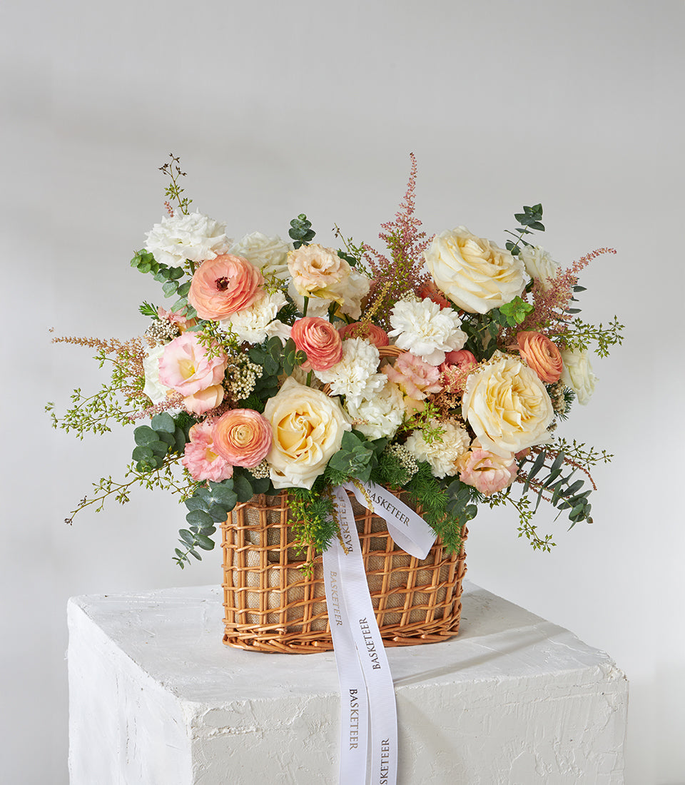 Peach and cream roses with white carnations in woven wicker gift basket, fresh flower arrangement