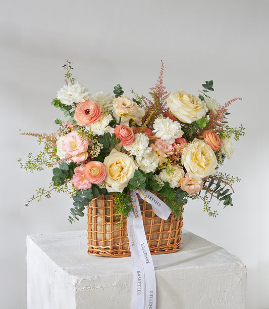Peach and cream roses with white carnations in woven wicker gift basket, fresh flower arrangement