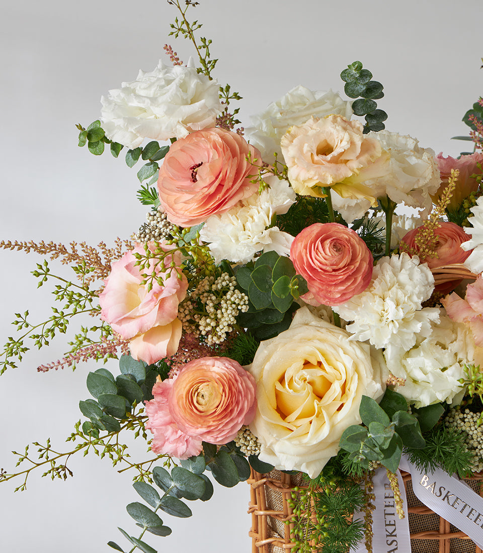 Peach and cream roses with white carnations in woven basket bouquet