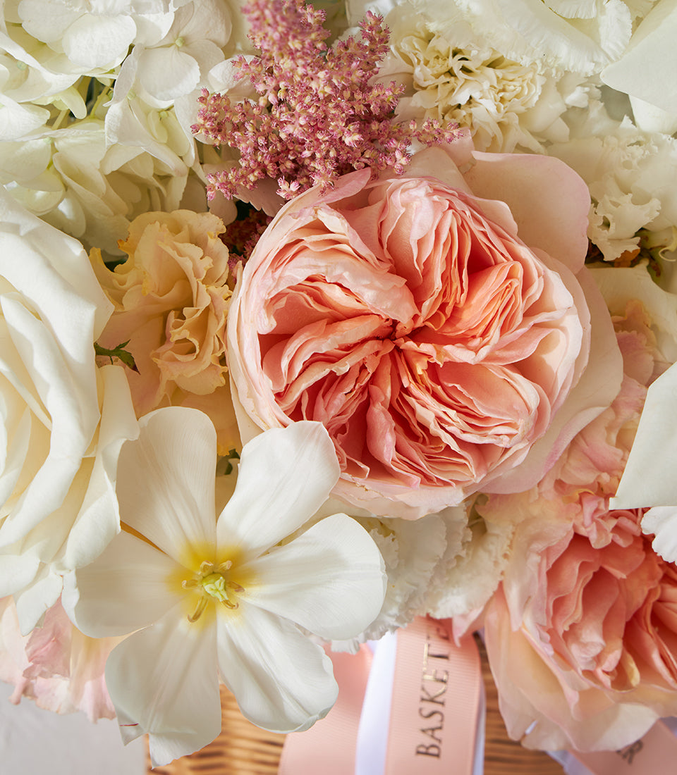 Peach garden roses and white roses in woven basket with hydrangeas and tulips