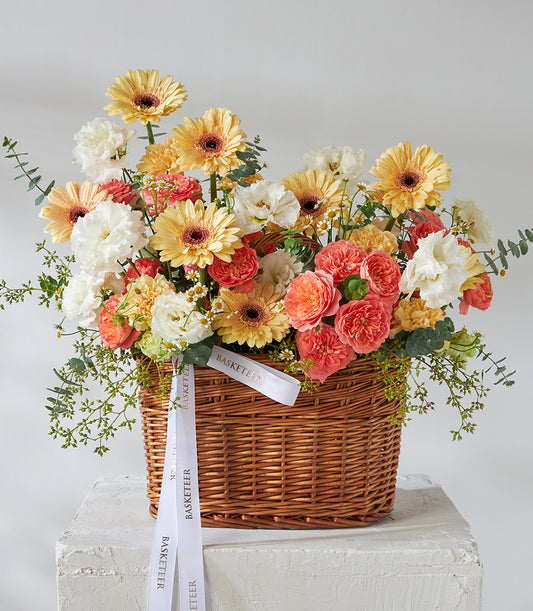 Peach roses, yellow gerberas, and white carnations in wicker basket with green foliage, birthday flowers