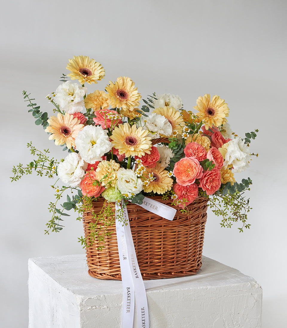 Peach roses, white carnations and yellow gerbera flowers in woven wicker basket for birthday