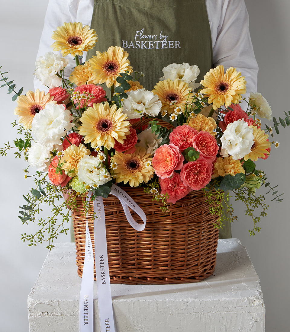 Peach roses, white carnations and yellow gerbera in woven wicker birthday flower basket