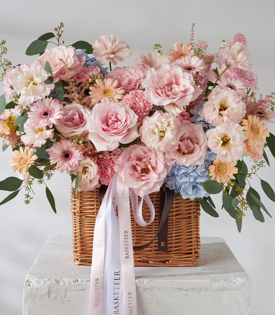 Pink roses, carnations and gerbera daisies in woven wicker basket with eucalyptus greenery