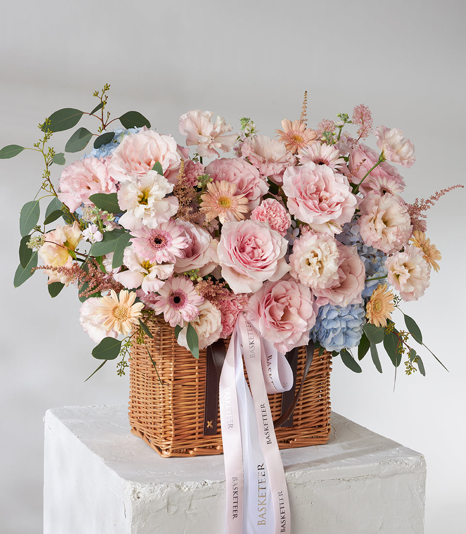 Pink roses, gerberas and carnations in wicker basket with eucalyptus greenery, premium fresh flower gift