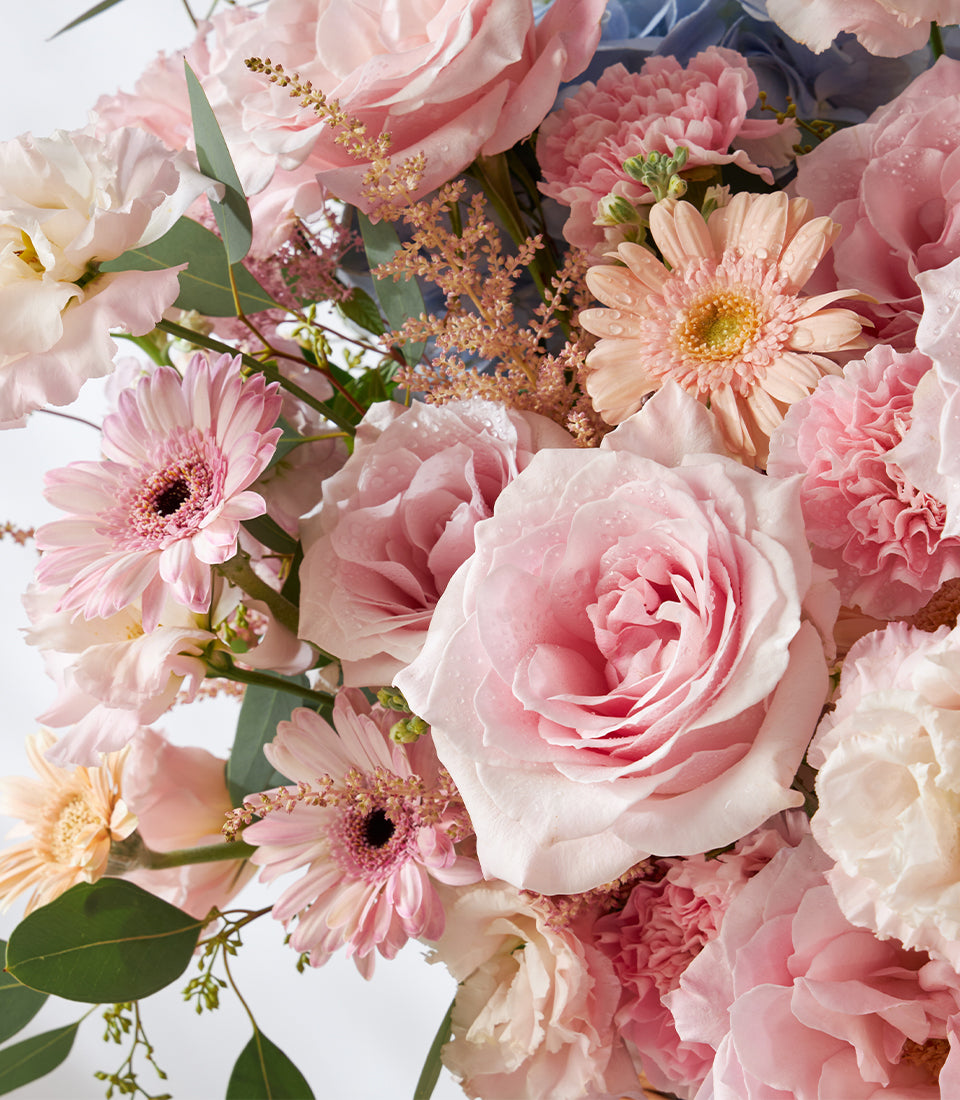 Pink roses, gerbera daisies, and carnations with eucalyptus in woven basket arrangement