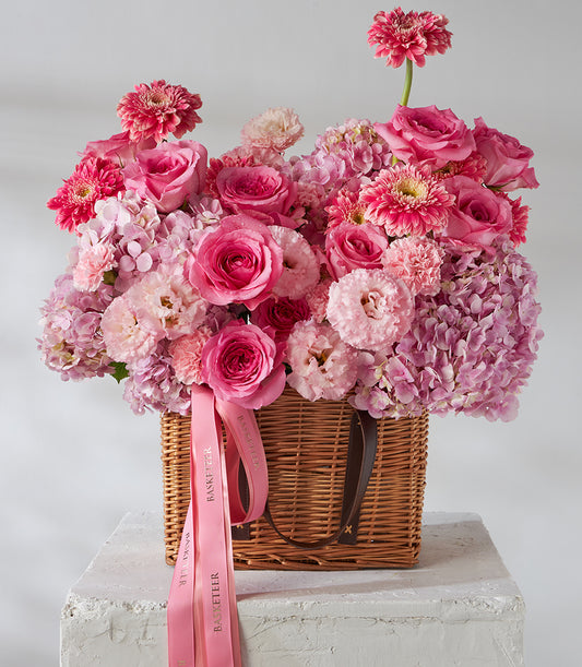 Hot pink roses, gerberas and hydrangeas in woven wicker basket with pink ribbons