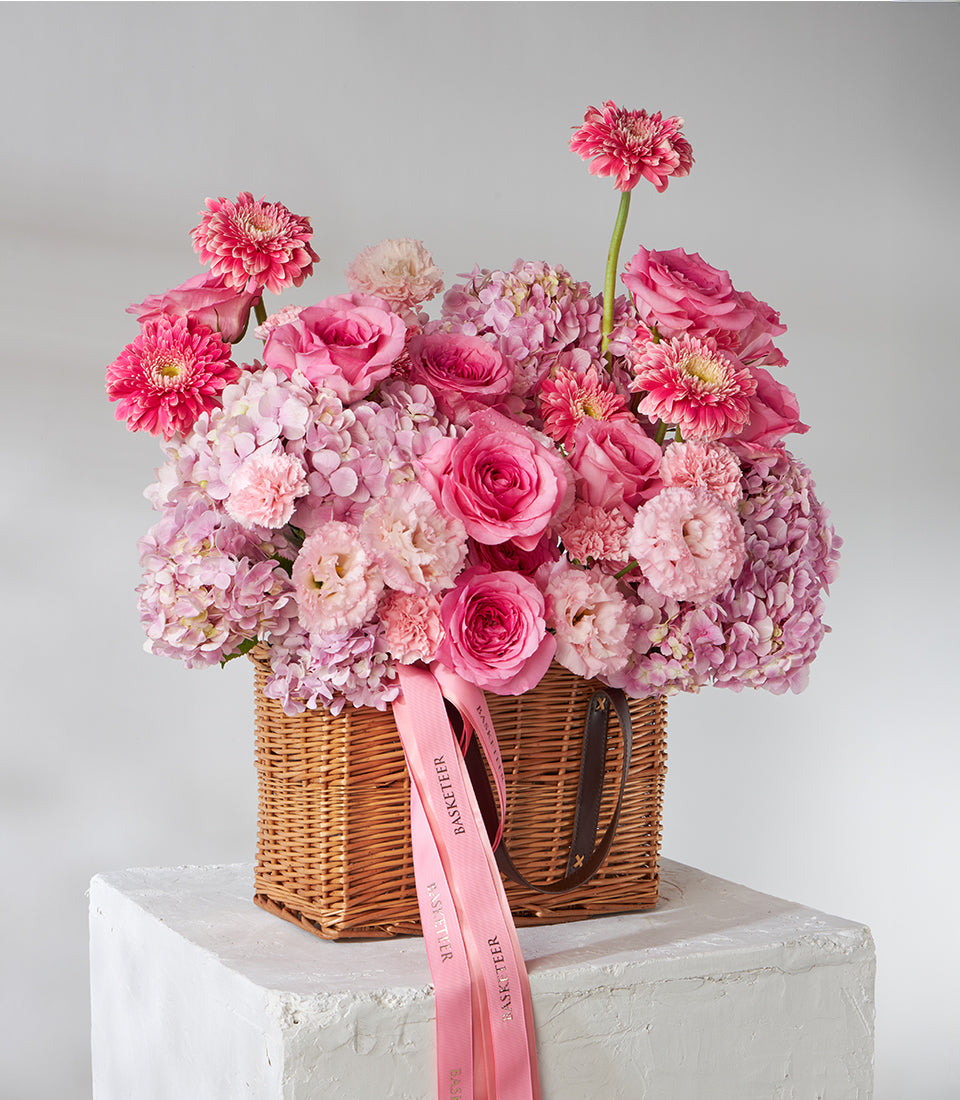 Hot pink roses, gerberas and hydrangeas in woven wicker basket with pink ribbons